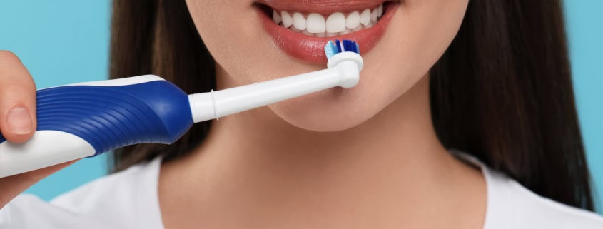 Mujer cepillándose los dientes con cepillo de dientes eléctrico - cuidado bucal en casa