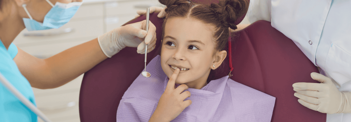 Salud bucal en niños: sellado dental y otros métodos de prevención 1 Odontopediatra enseñando un modelo dental a una niña pequeña durante su primera visita al dentista en Clínica Dental Benalúa Alicante