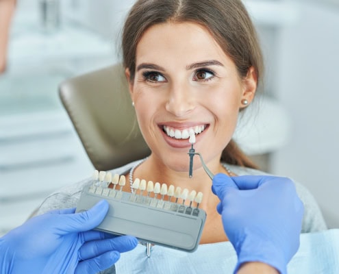 Paciente sonriendo junto a una guía de color dental durante el diseño de carillas dentales en Clínica Dental Benalúa Alicante