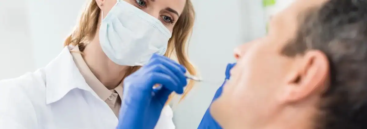 Causas y Tratamiento de los Dientes Negros 1 Dentista revisando los dientes de un paciente con espejo dental en la consulta