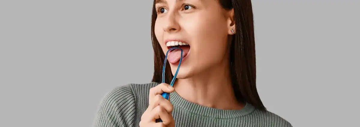 Mujer usando un limpiador lingual para limpiar la lengua