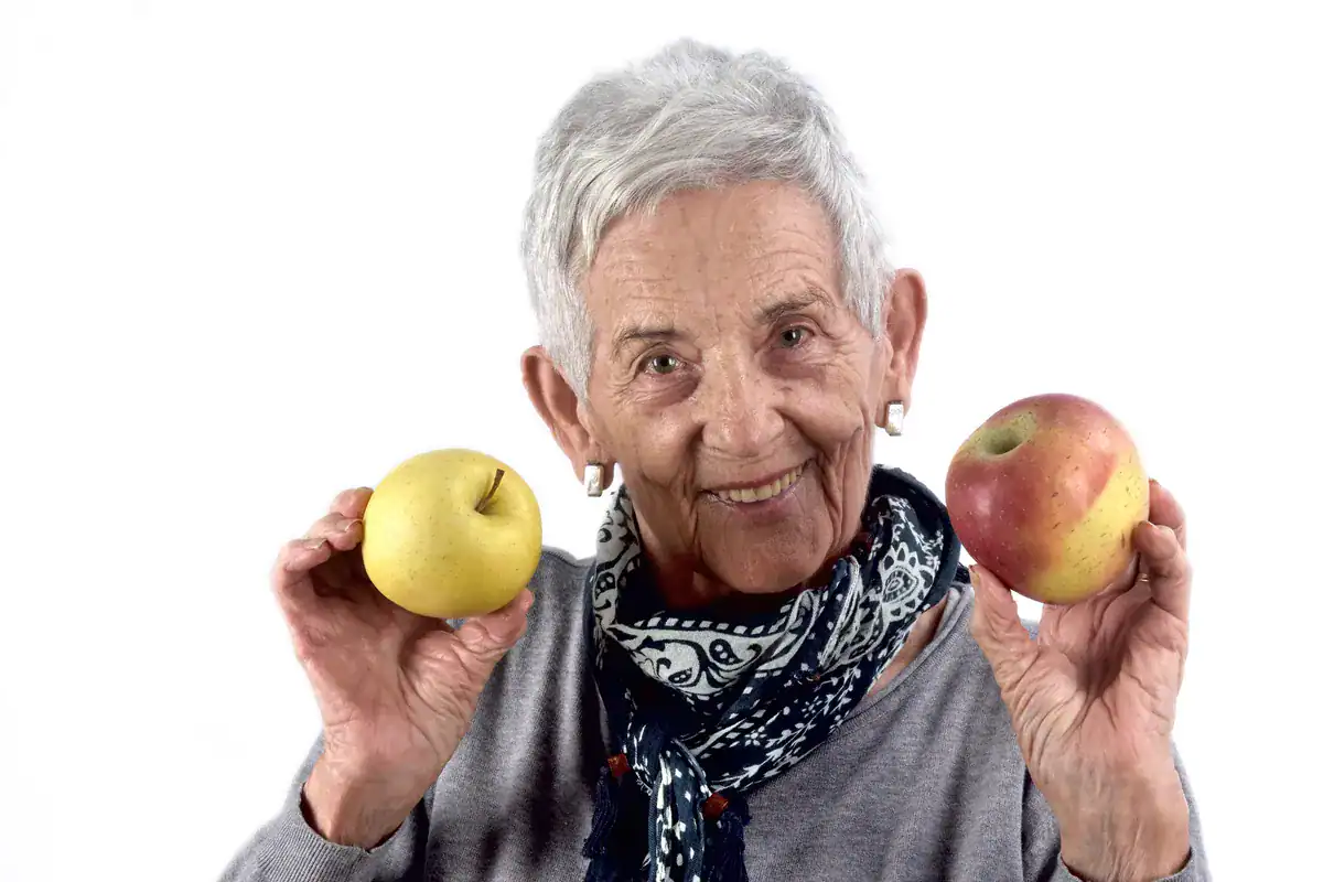 Mujer mayor sonriendo con una manzana en cada mano