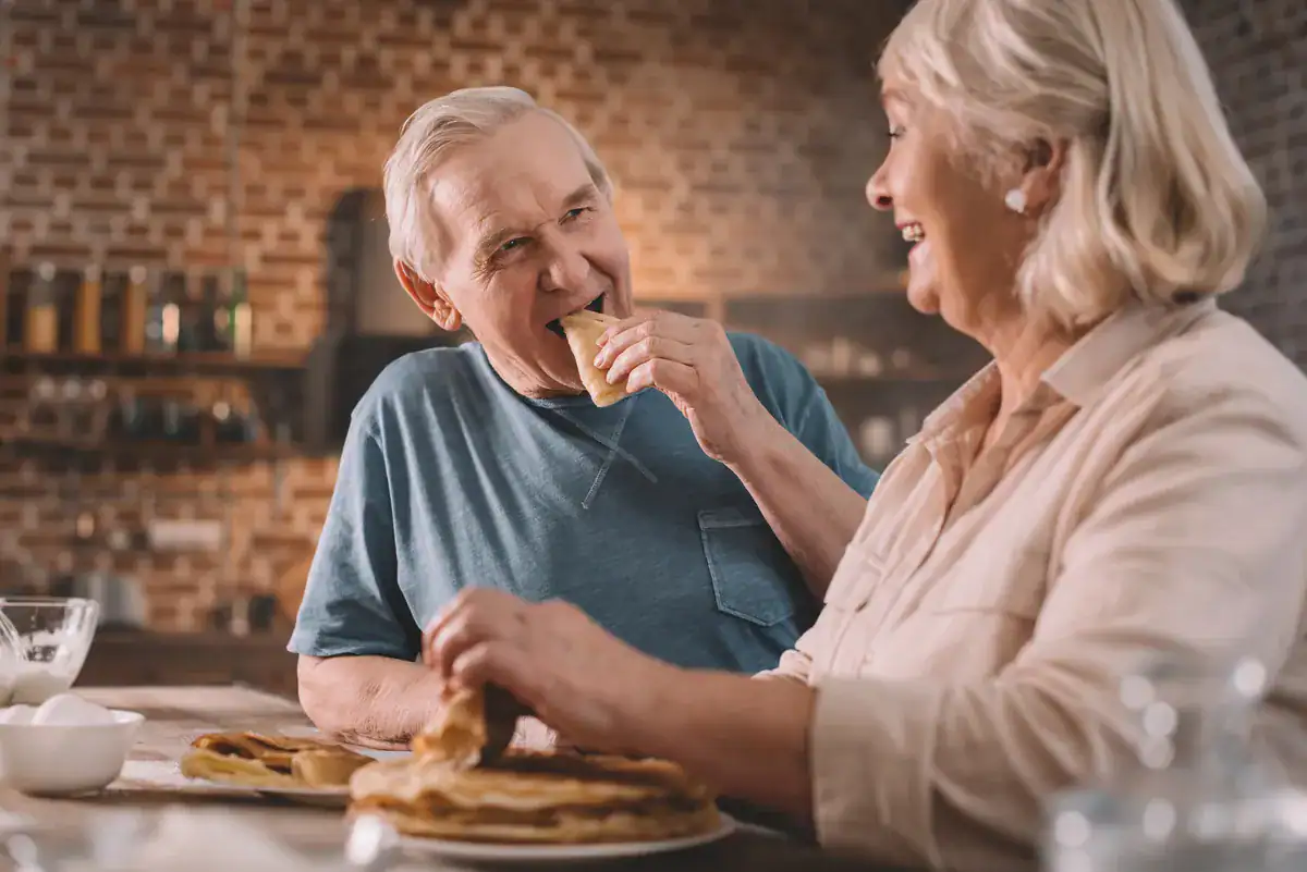 Pareja mayor comiendo y sonriendo en casa
